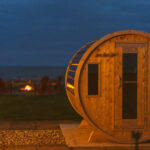 Wood barrel sauna in the evening with fire and Lake Erie in the background