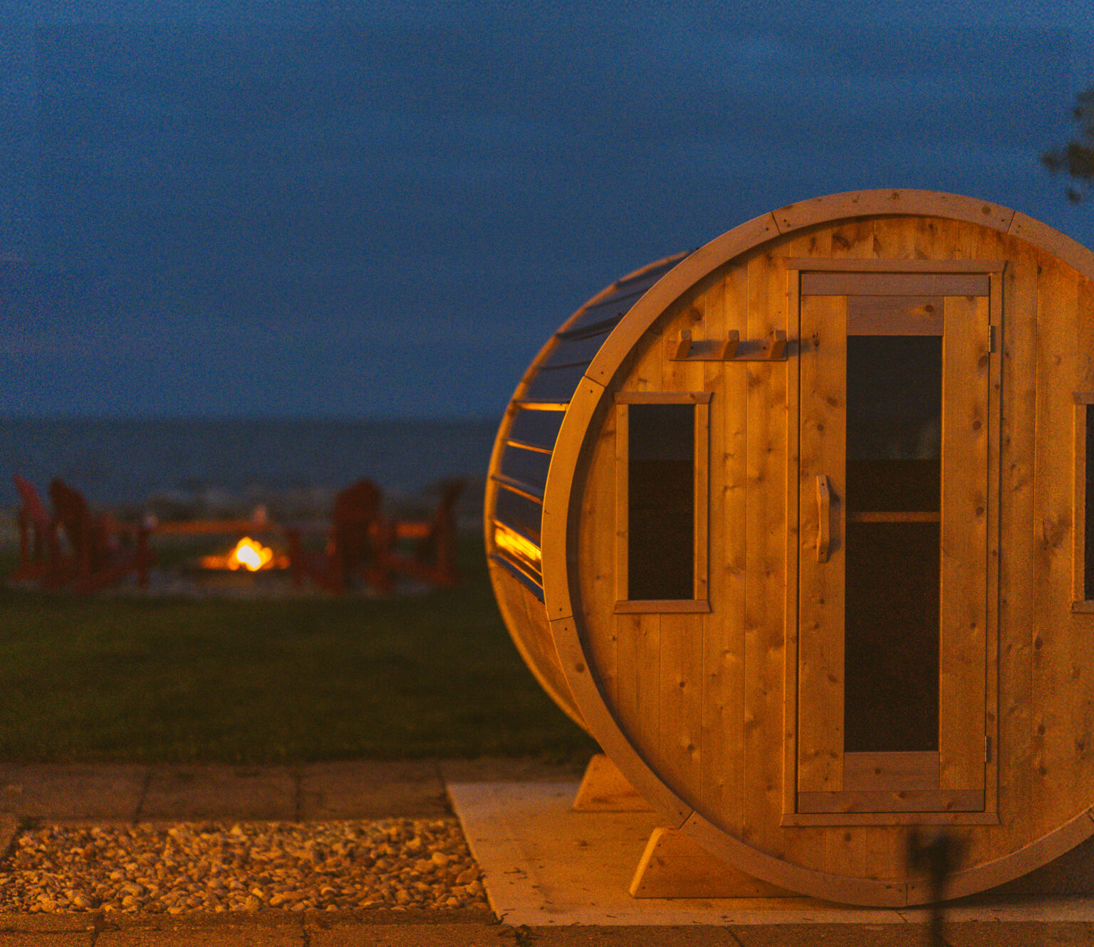 Wood barrel sauna in the evening with fire and Lake Erie in the background