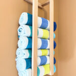 Beach towels, blue, white and yellow striped, rolled in a wooden holder on the wall.