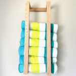 Beach towels, blue, white and yellow striped, rolled in a wooden holder on the wall.