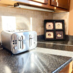 4 slice stainless steel toaster on dark kitchen counter with tray in background.